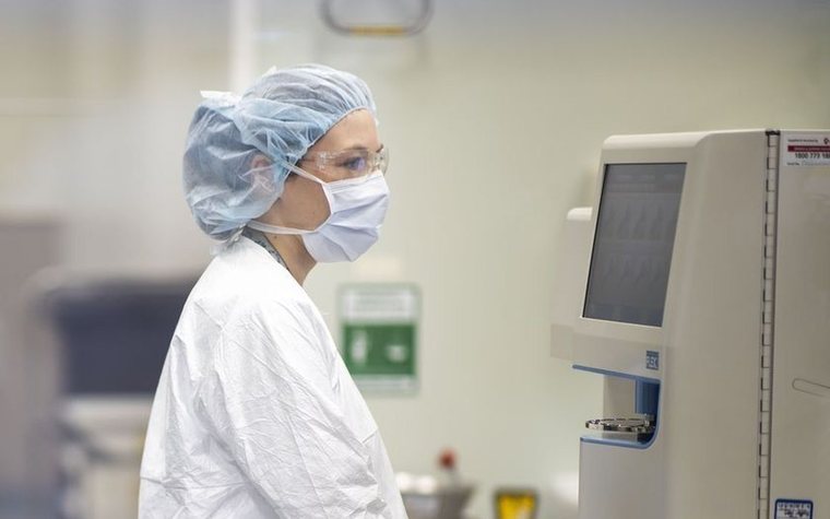 Gowned NBF operator running an instrument in the clinical-grade manufacturing suite